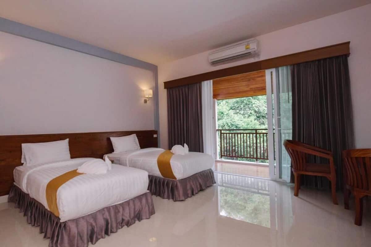 Une chambre d’hôtel avec deux lits, un balcon, un bureau en bois et un appareil de climatisation.