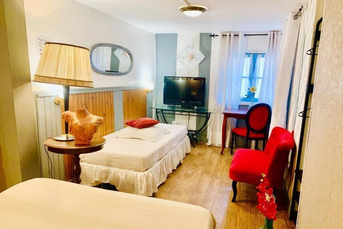 Quarto de hotel com cama, escrivaninha com cadeira, televisão e luminária.