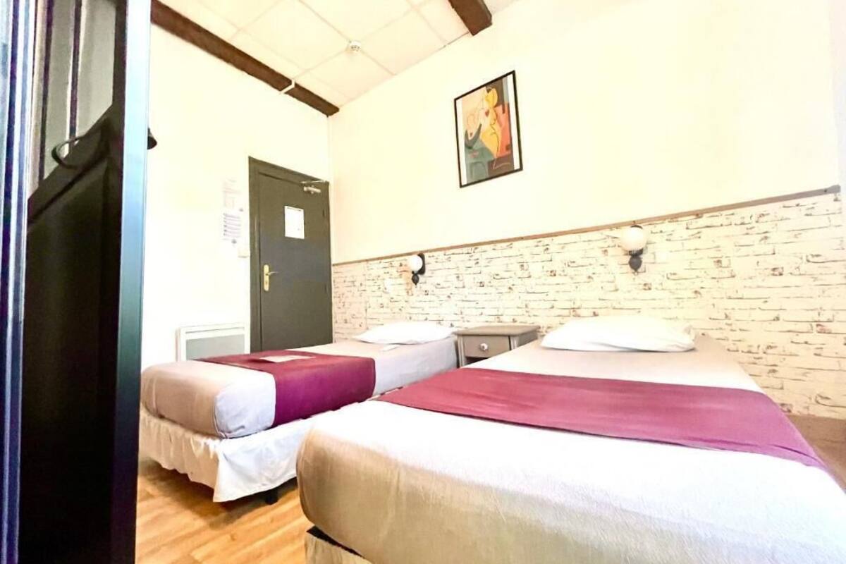 Um quarto com duas camas, parede de tijolos, uma porta e um quadro na parede.