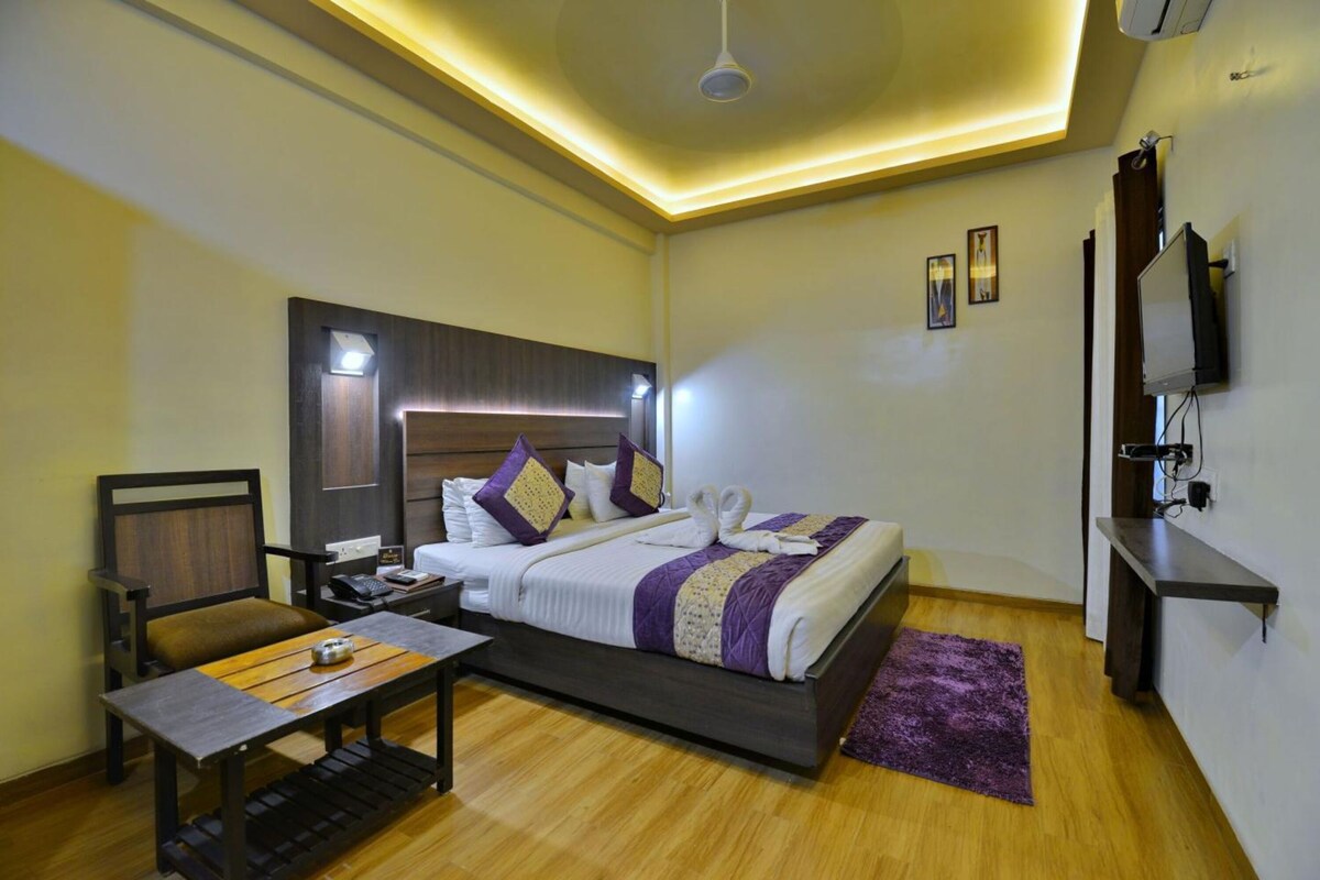 Une chambre d’hôtel équipée d’un lit, d’une table de chevet, d’une chaise, d’un bureau et d’un téléviseur fixé au mur.