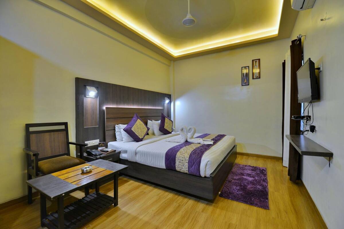 Ein Hotelzimmer mit Bett, Nachttisch, Stuhl, Schreibtisch und einem an der Wand befestigten Fernseher.