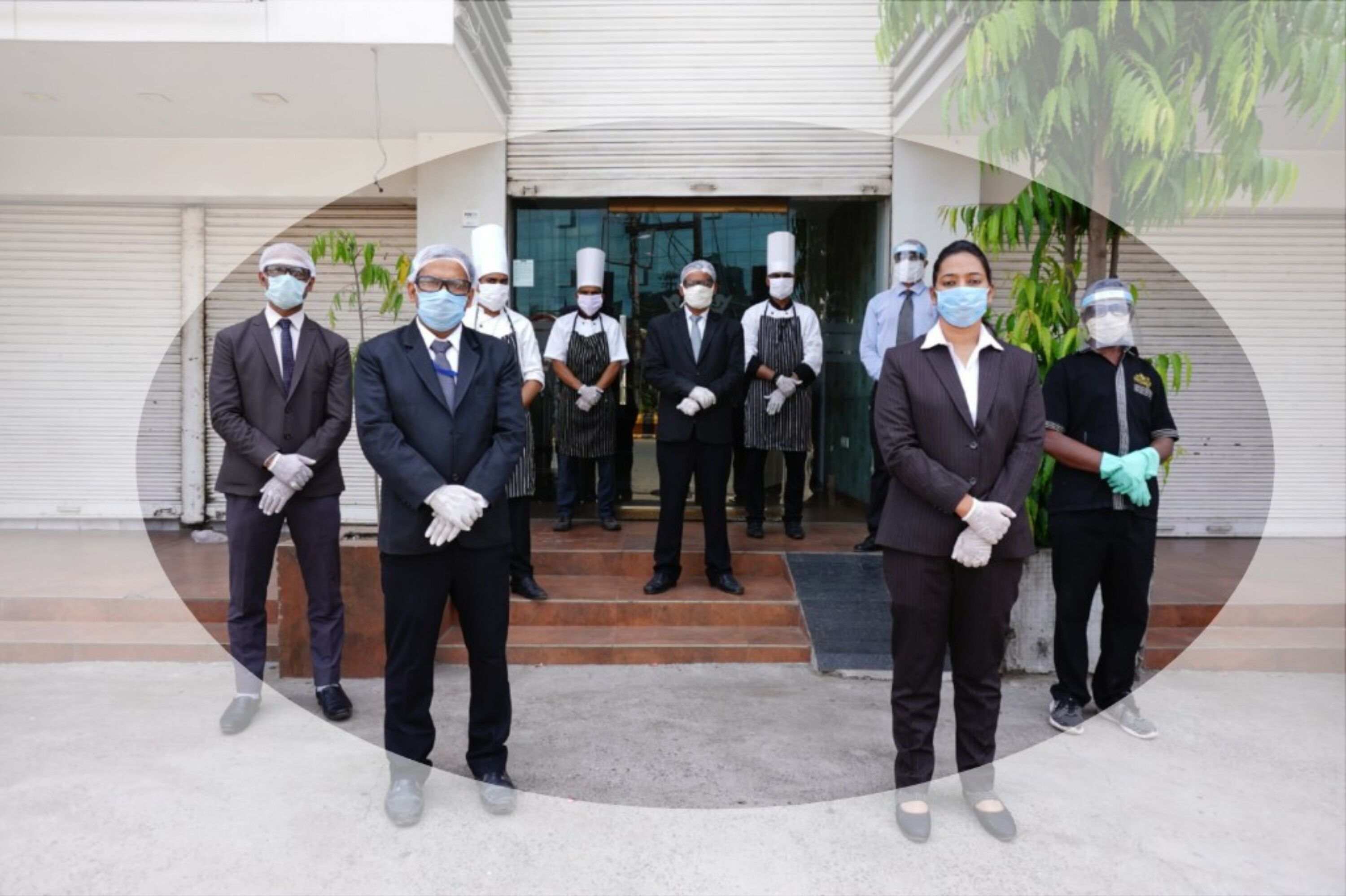A group of people in formal attire standing in front of a building with a closed shutter door.