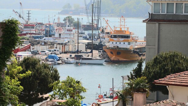 Un port de plaisance où sont amarrés divers bateaux, dont un grand navire orange, le tout entouré de verdure et de bâtiments.