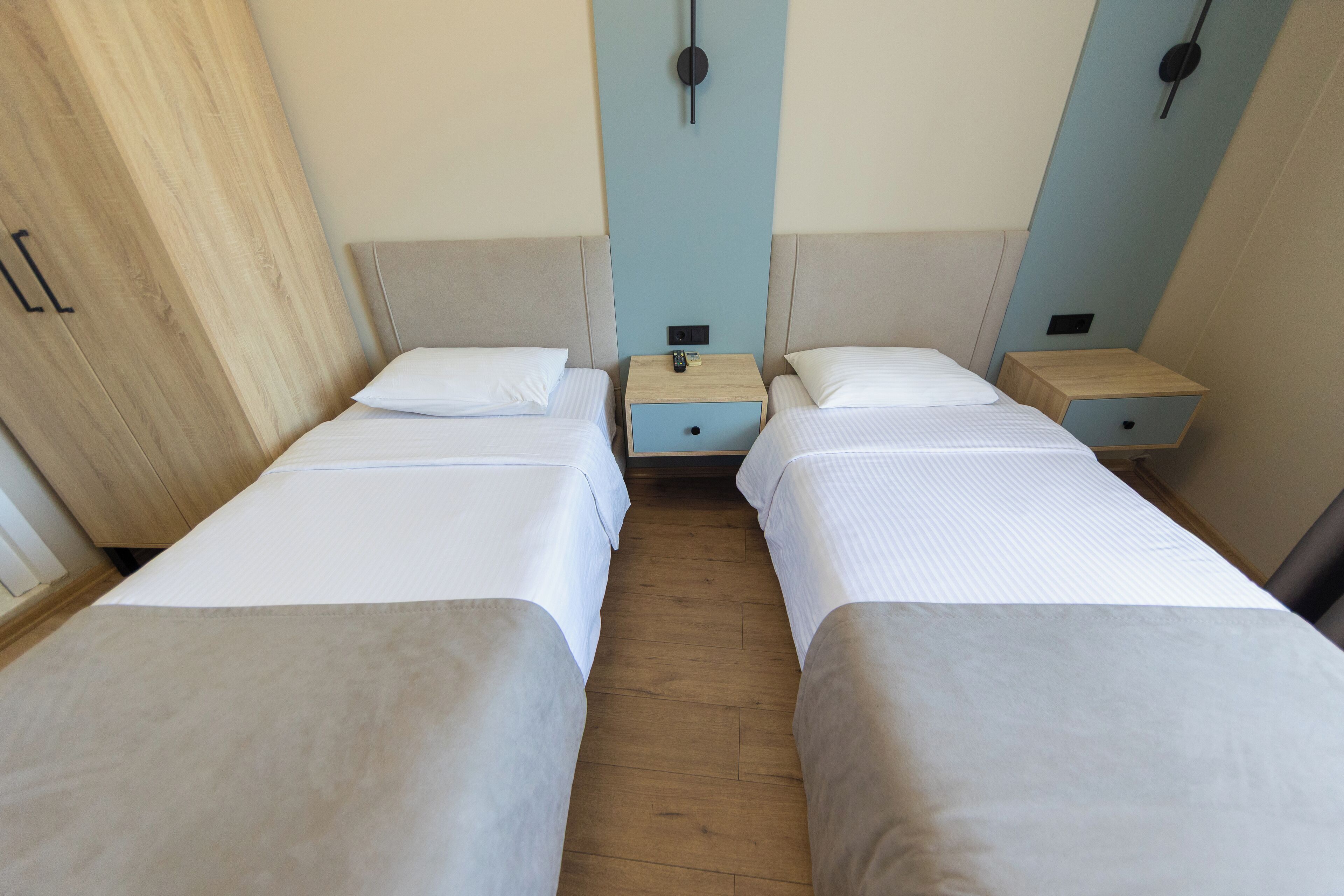 A room with two single beds, wooden nightstands, and a wardrobe.