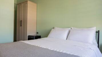 Una cama bien hecha con sábanas blancas, una mesita de noche y un armario en una habitación con paredes verde claro.