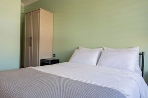 Una cama bien hecha con sábanas blancas, una mesita de noche y un armario en una habitación con paredes verde claro.