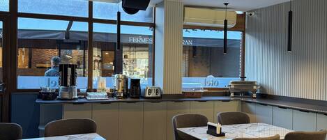 A modern restaurant interior with marble-topped tables, cushioned chairs, and a view of the street through large windows.