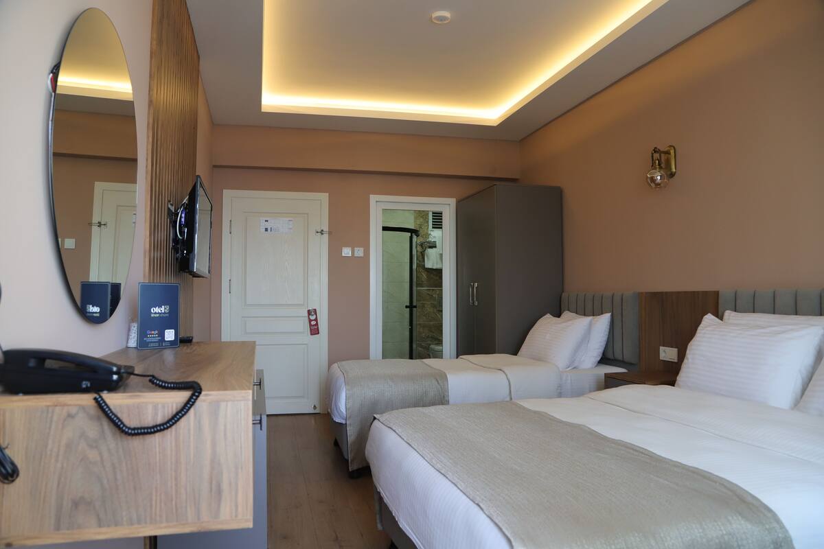A hotel room with two beds, a wooden desk with a telephone, a minibar, and a mirror.