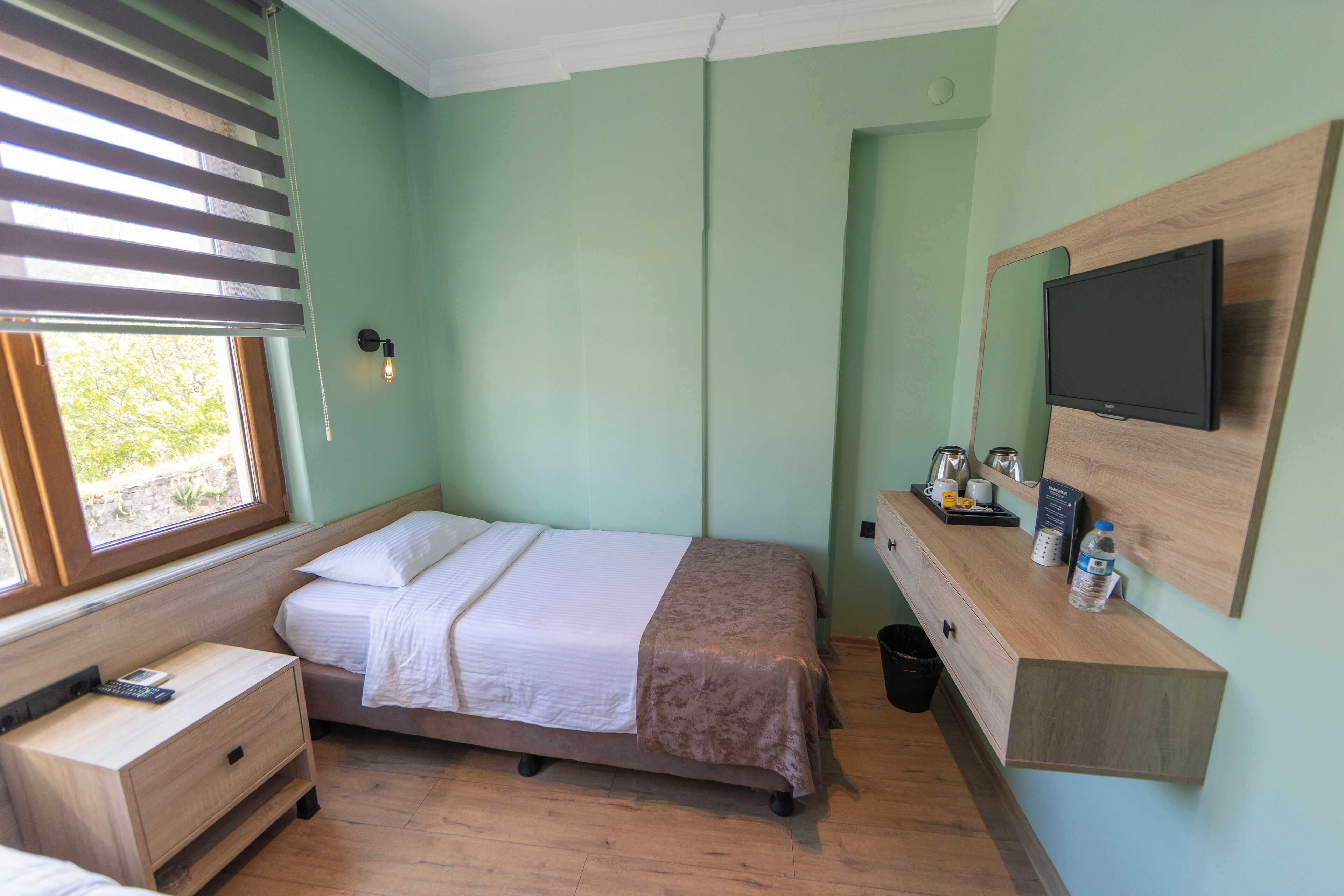 Un dormitorio con cama, mesita de noche, televisor y ventana con persianas.