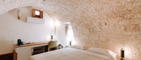 Un dormitorio con techo de piedra, una cama, un escritorio y una silla.