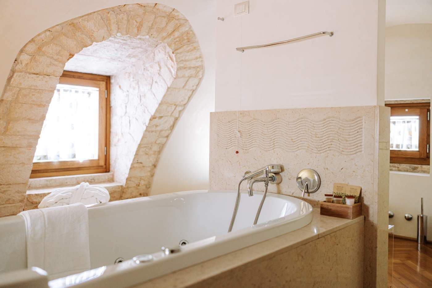 Un bagno con una vasca freestanding, una finestra con stipite in legno, un appendi asciugamani e un asciugamano sul pavimento.