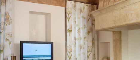 A room with a television on a wooden desk, a green chair, and a stone wall.
