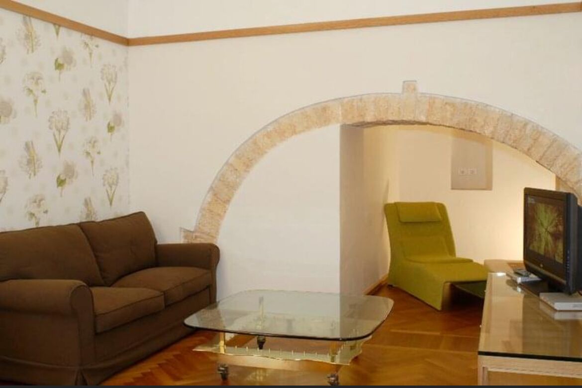 A living room with a brown sofa, a glass coffee table, a green armchair, and a TV on a stand.