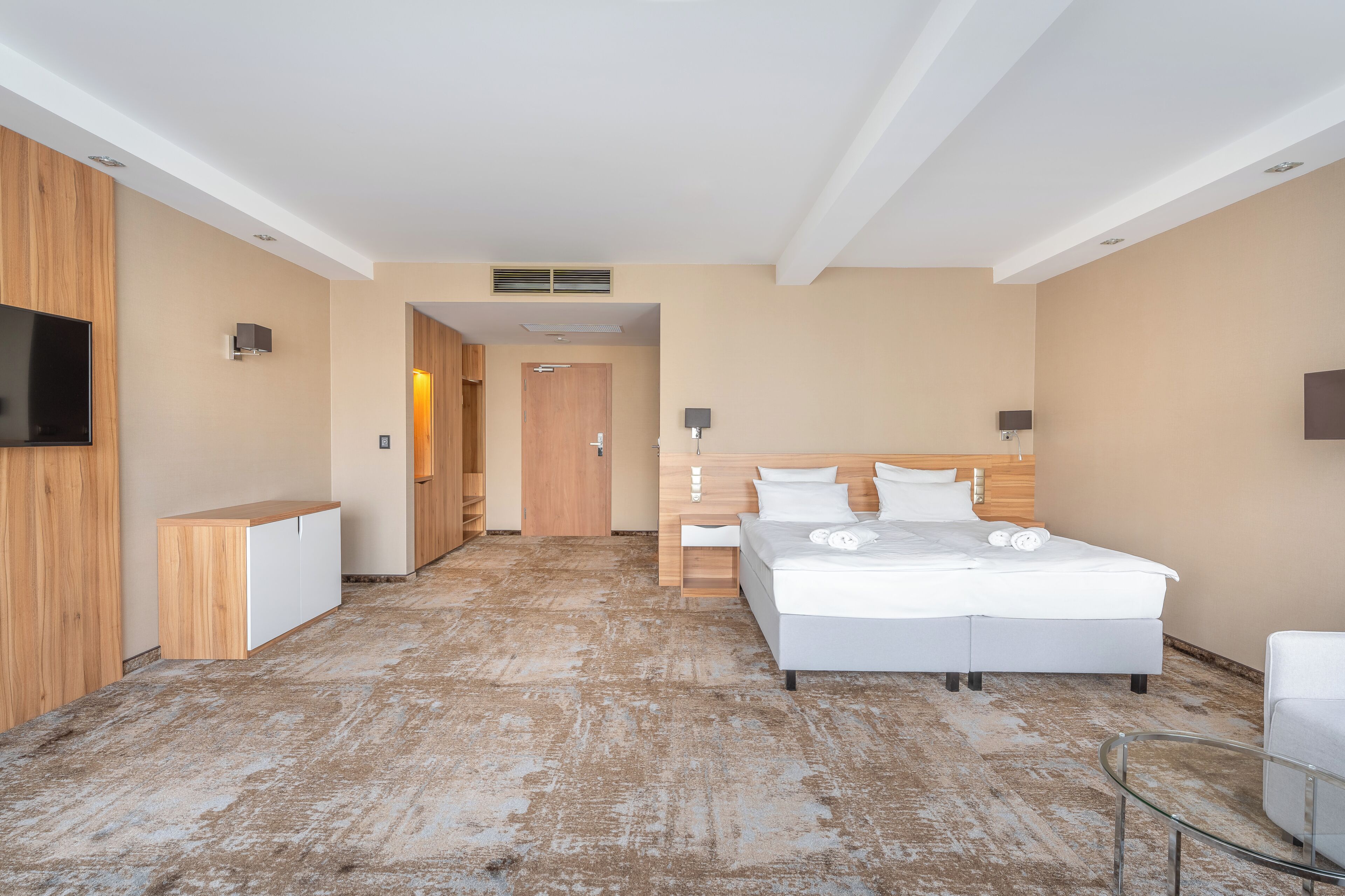 Una habitación de hotel moderna con una cama grande, un televisor, un armario de madera y una mesa de vidrio.