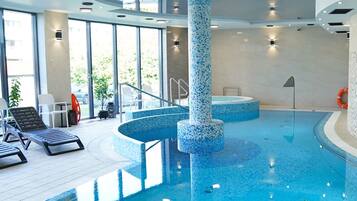 Una piscina interior con suelo de baldosas, una columna central y una zona soleada con sillones de descanso.