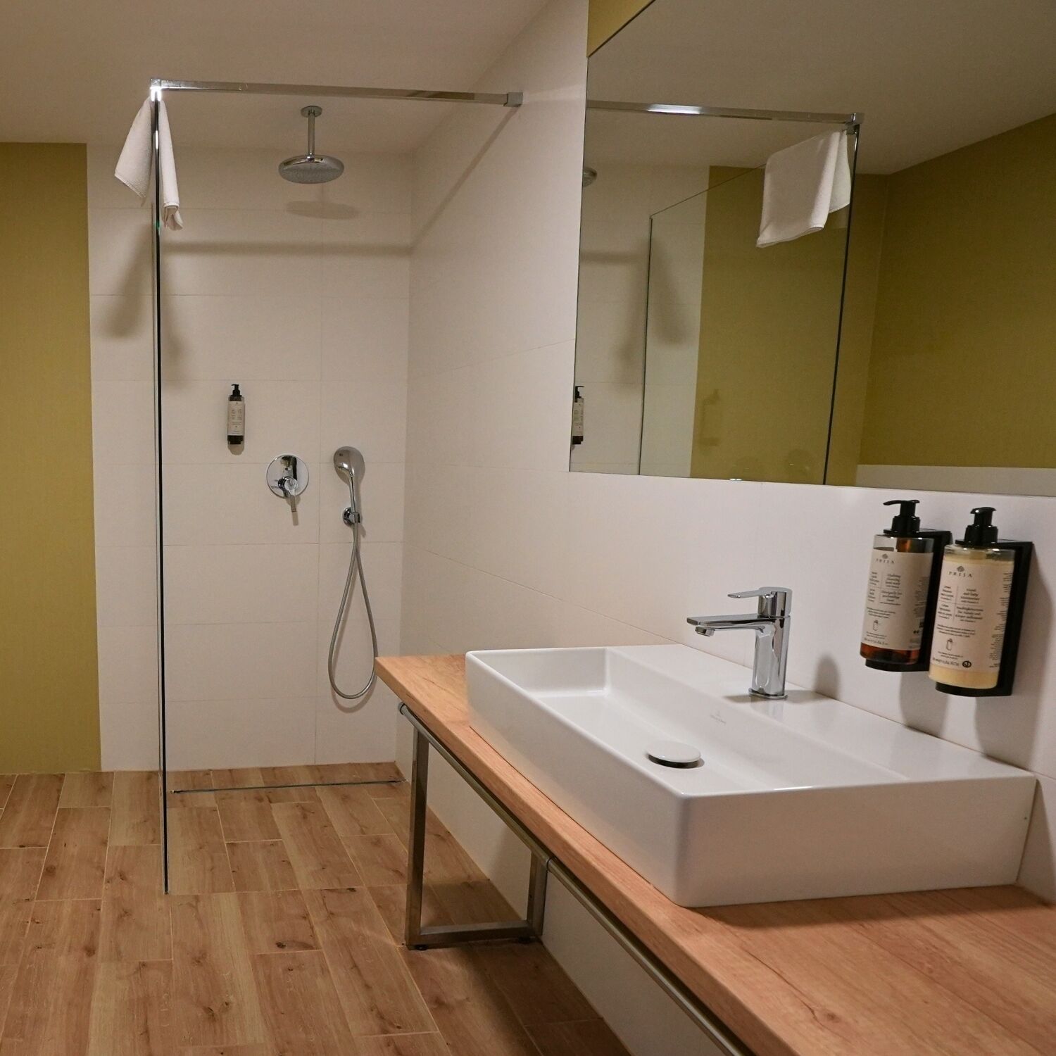 A modern bathroom with a white sink, a handheld showerhead, and two bottles of toiletries on the wall.