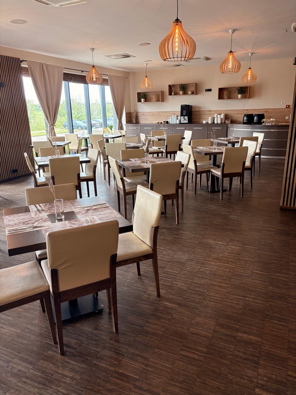 A dining area with multiple tables and chairs, a kitchen in the background, and pendant lighting.