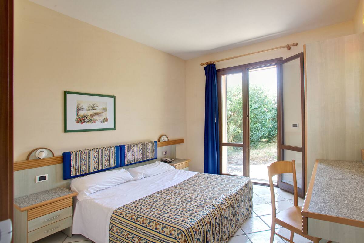 Une chambre à coucher comprenant un lit, des tables de chevet, une chaise, une fenêtre avec des rideaux et une porte donnant sur un balcon.