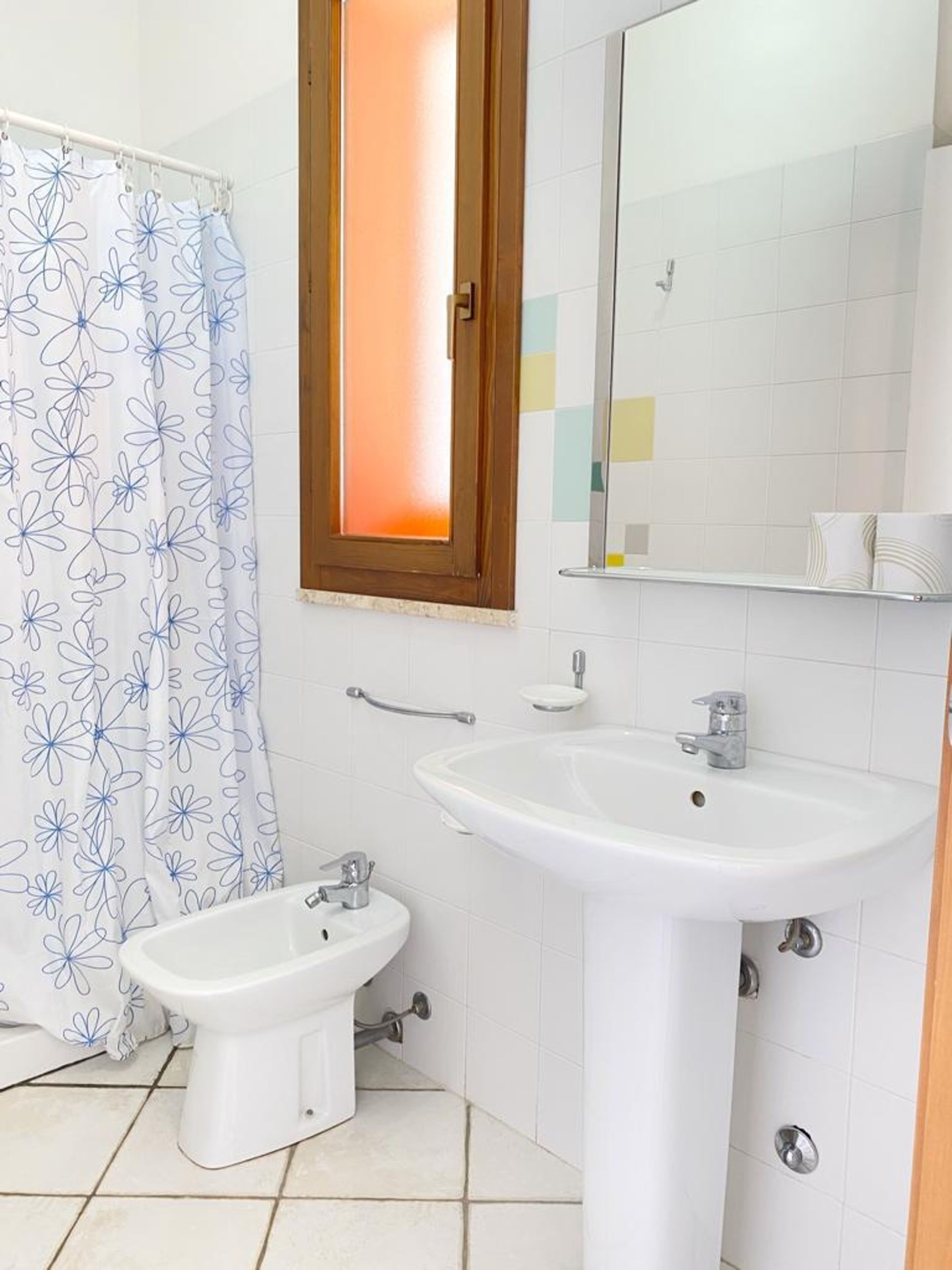 A bathroom with a shower, a bidet, a sink, and a mirror.