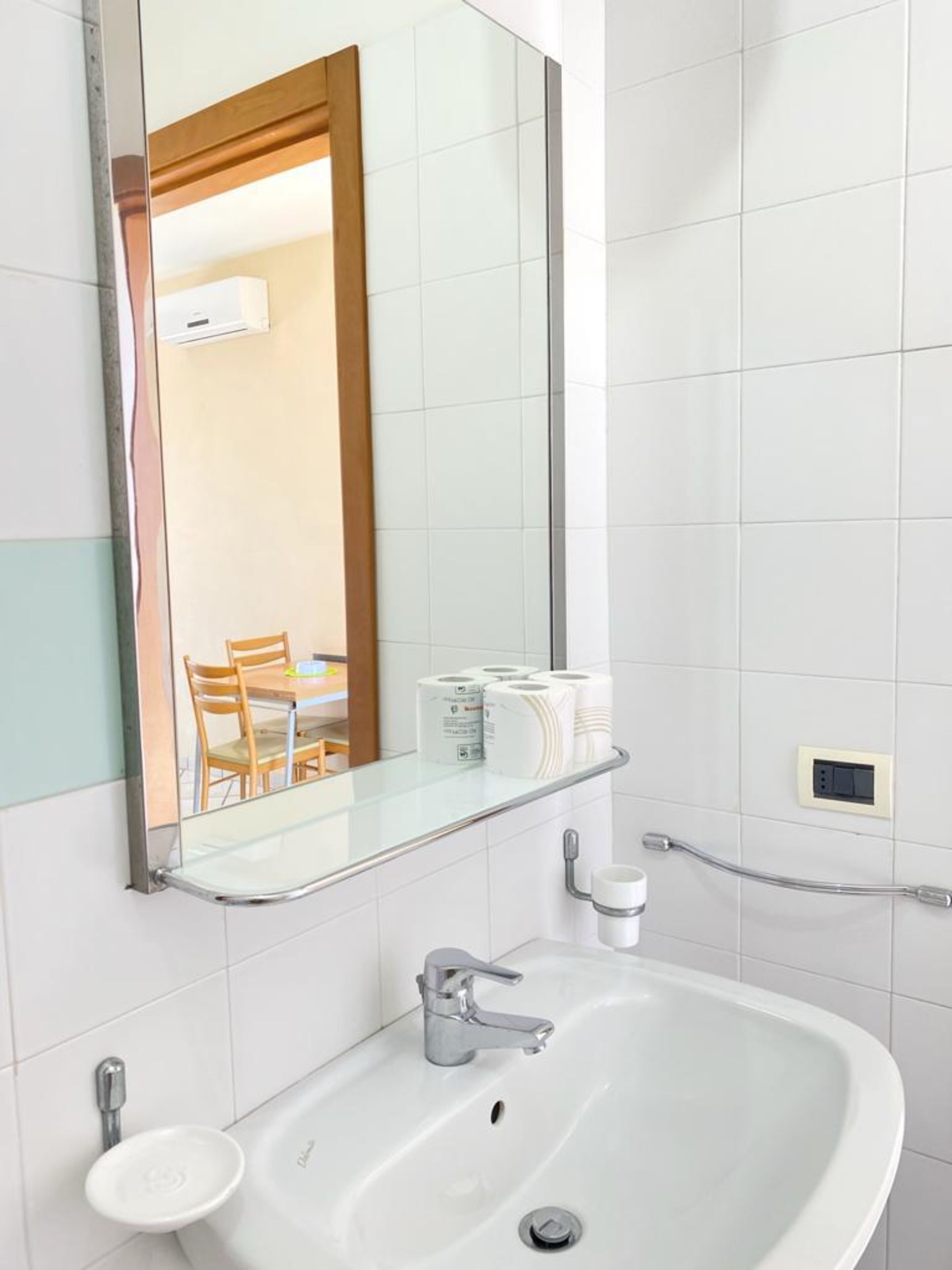 Een badkamer met een wit wastafelmeubel, een spiegel en een glazen plankje met toiletpapier.