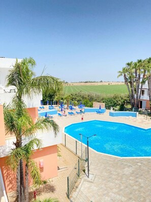 A swimming pool with lounge chairs and palm trees, surrounded by a fence.