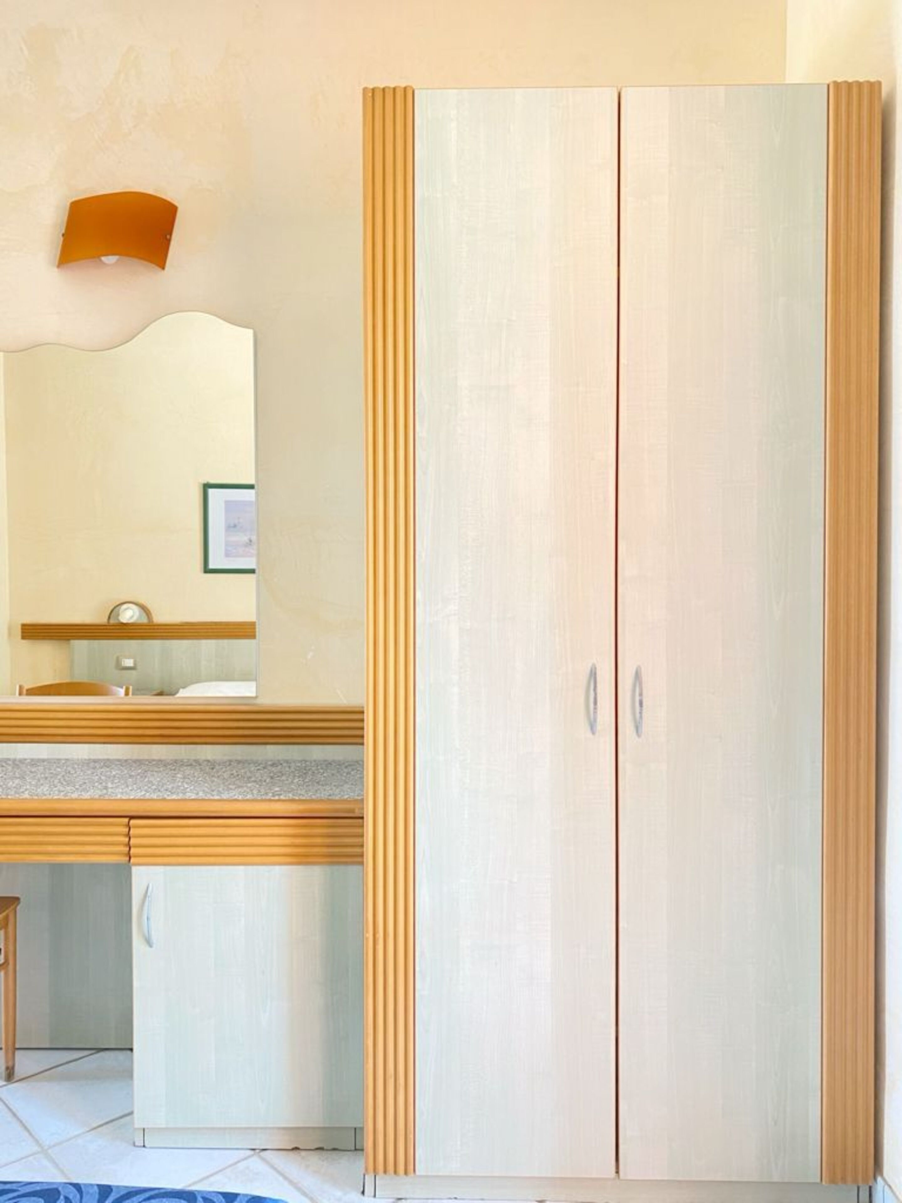 A bedroom with a double wardrobe, a bedside table, and a mirror.