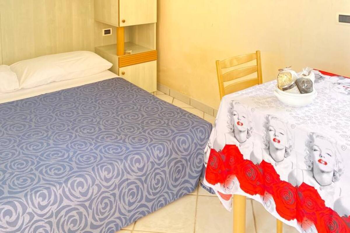 Une chambre à coucher comprenant un lit, une armoire, une table à manger avec des chaises et un luminaire suspendu.