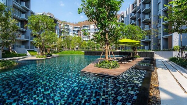 Un hotel moderno con una piscina central, rodeado de exuberante vegetación y varios balcones.
