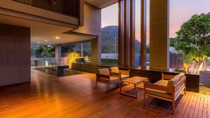 Un espacio exterior moderno con suelo de madera y mobiliario, amplias ventanas que ofrecen vistas a un paisaje montañoso.