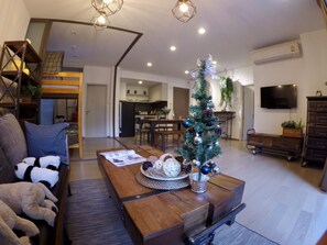 Een moderne woonkamer met een houten salontafel, een kleine kerstboom en een bank met kussens.