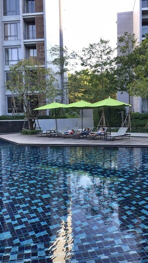 A swimming pool with a tiled pattern, surrounded by lounge chairs and green umbrellas.