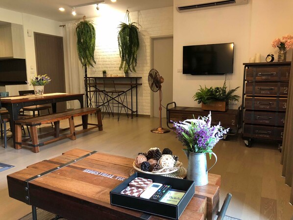 A modern living room with a wooden coffee table, a TV mounted on the wall, and a dining area with a table and chairs.