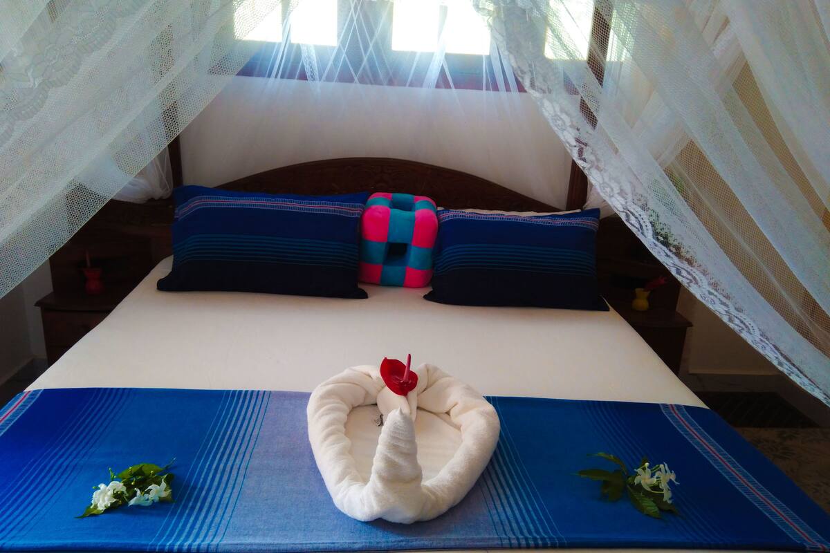 Ein Bett mit blauer Bettdecke, weißen Kissen und einer dekorativen Schwaneinrichtung.