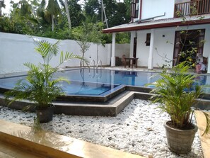 A swimming pool with a white wall and a balcony. There are potted plants around the pool. - Galle Cemellia (Hapugala)