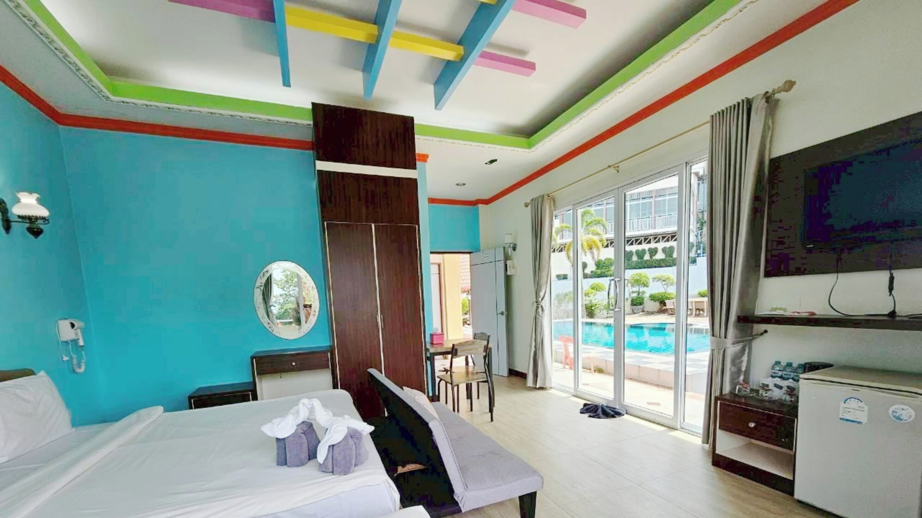 Quarto de hotel com cama, escrivaninha, cadeira, televisão e vista para uma piscina.