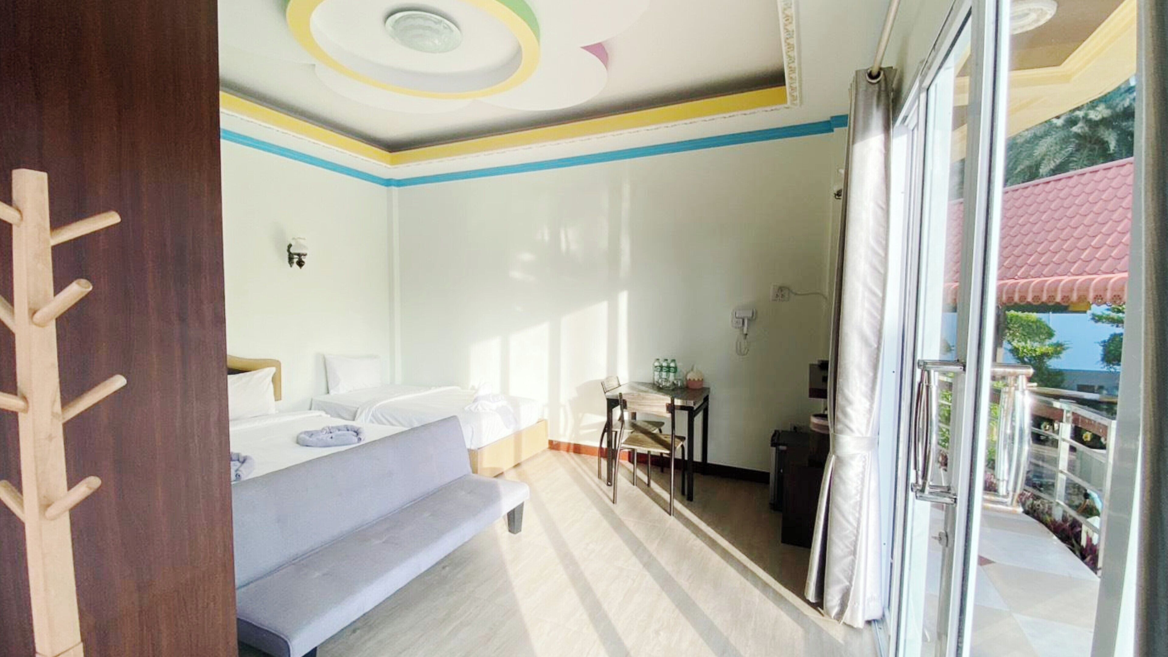 Una habitación de hotel con cama, un banco, una mesa con botellas y vistas al exterior.