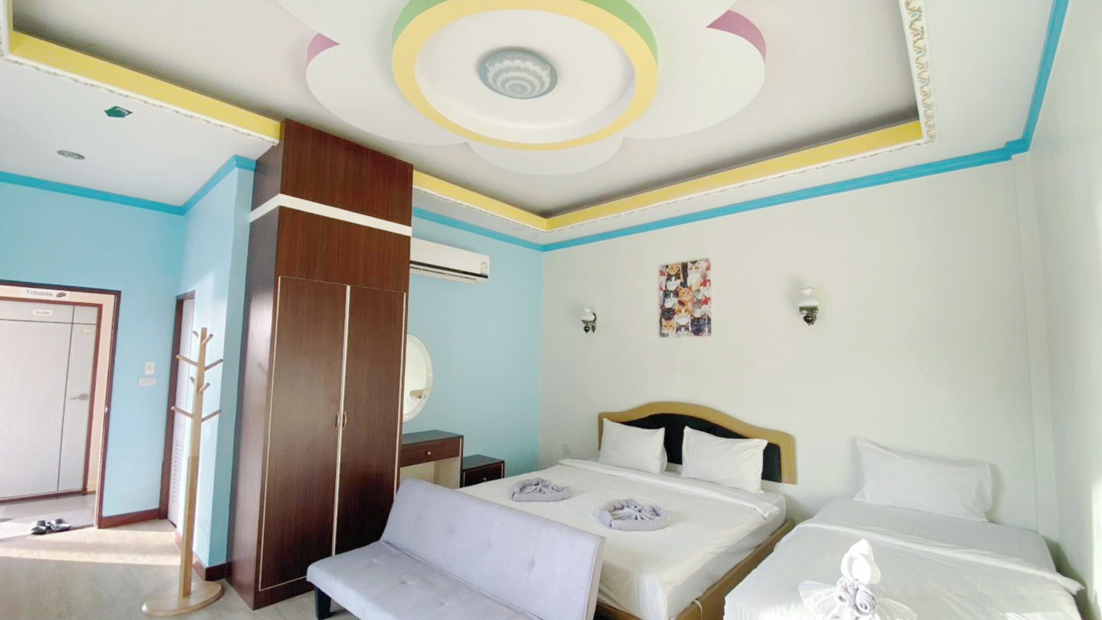 A hotel room with a bed, a bench, a wardrobe, and a ceiling with a circular design.