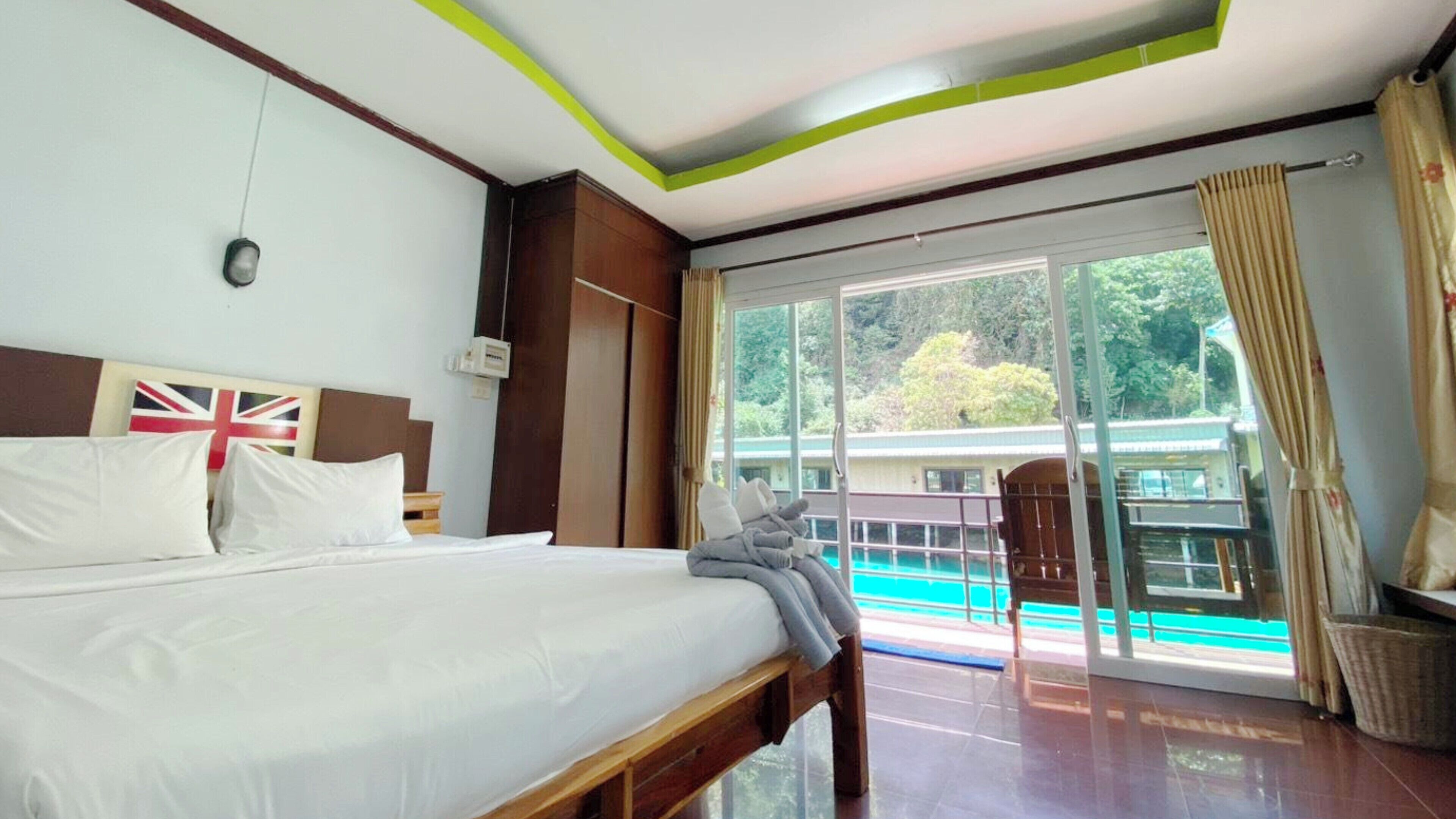 A hotel room with a bed, a flag decoration, a window with a view of a pool, and a door leading to an outdoor area.
