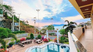 A swimming pool with a view of the sky and mountains, surrounded by outdoor seating and greenery. - Laketerrace Resort (La-ngu)