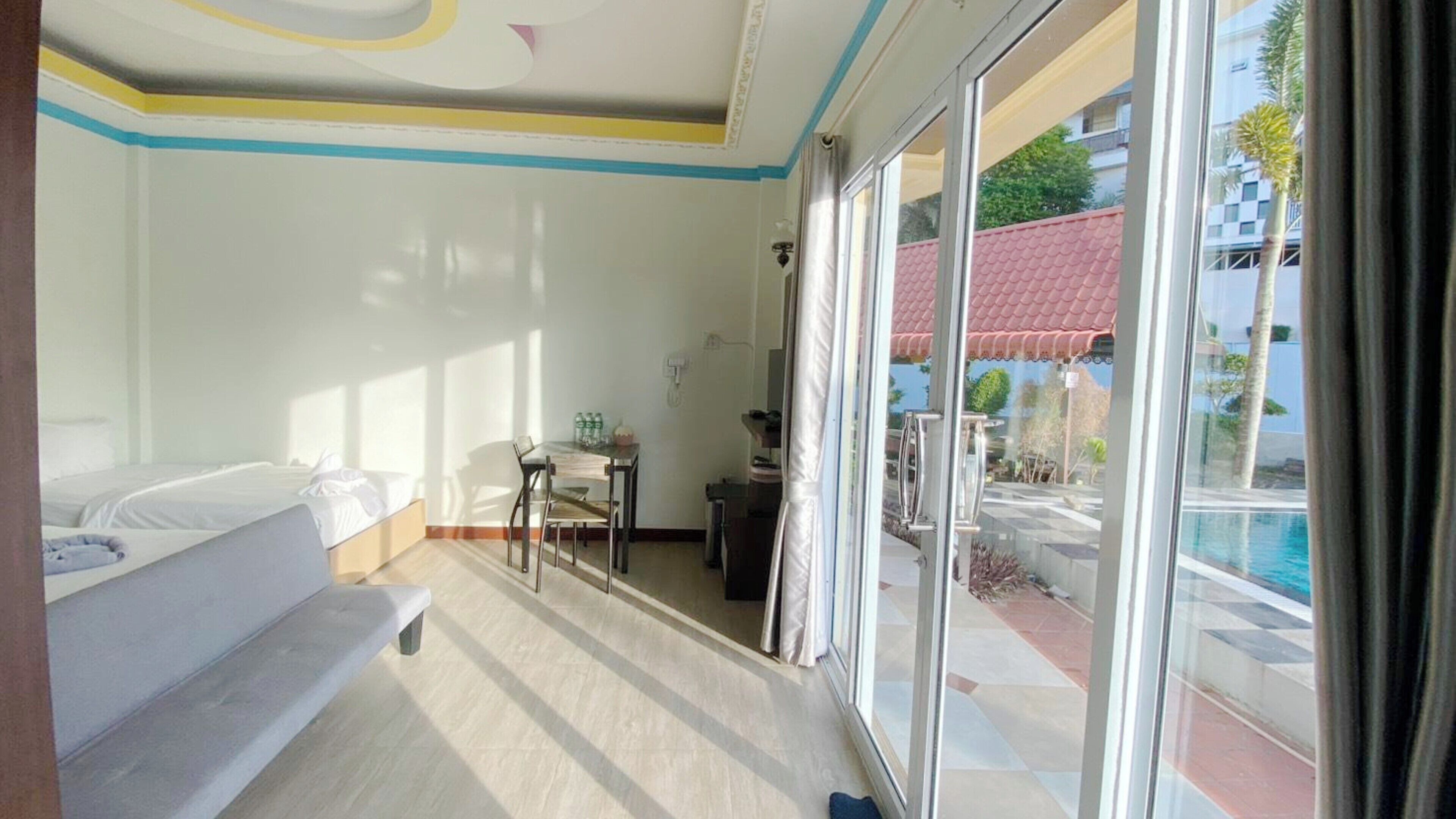 A hotel room with a bed, a small table with chairs, a desk, and a view of a swimming pool through large windows.