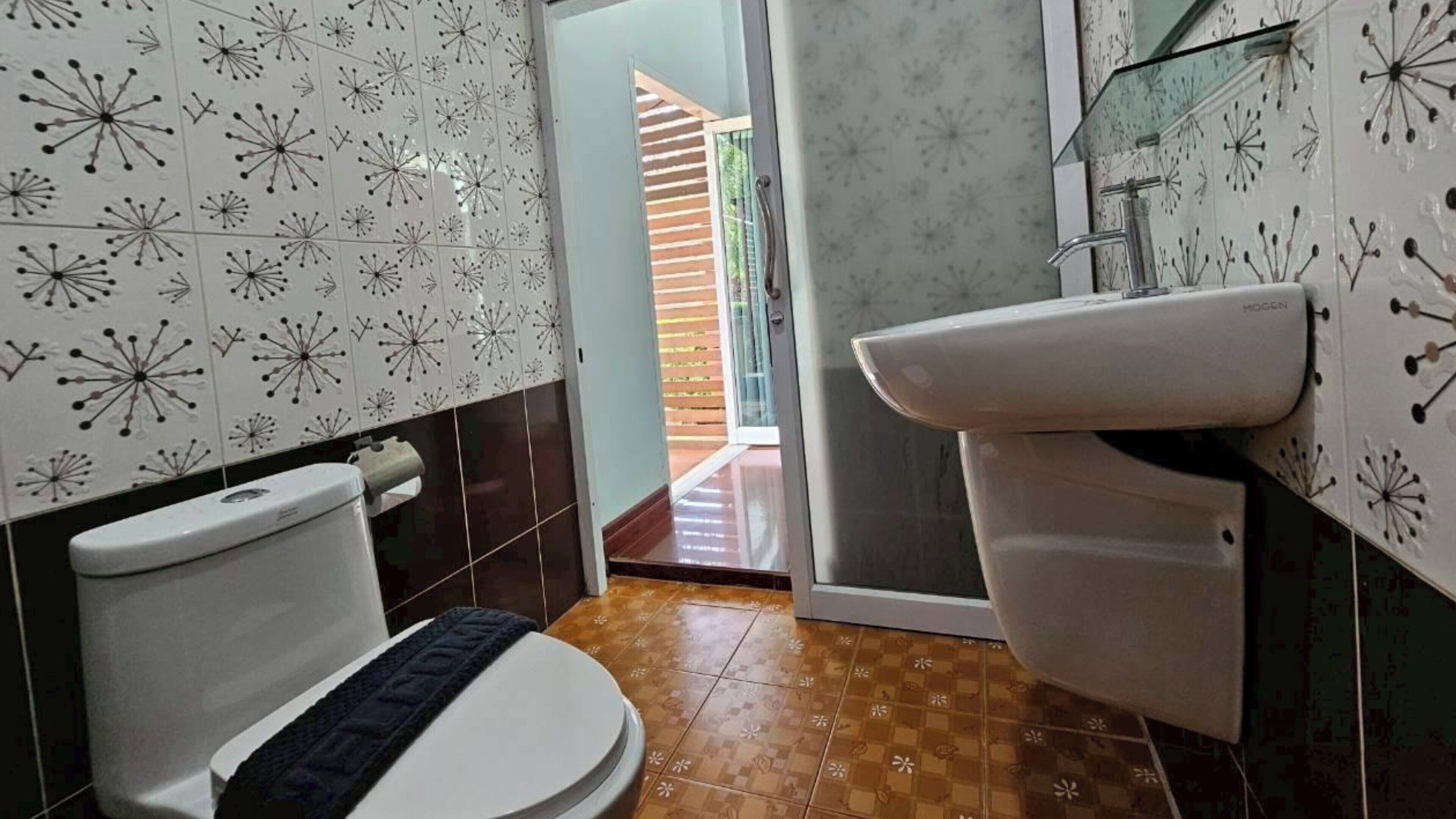 A bathroom with a toilet, sink, and patterned tiles.