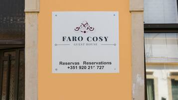 A sign for 'FARO COSY GUEST HOUSE' with a contact number for reservations.