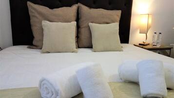A neatly made bed with rolled white towels, a dark headboard, and two bedside tables with a lamp and water bottles.