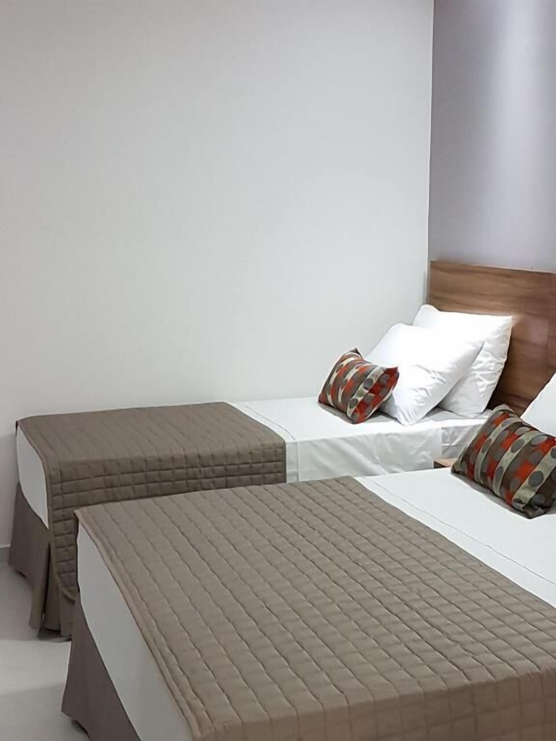 A hotel room with two beds, each with a quilted headboard and pillows.