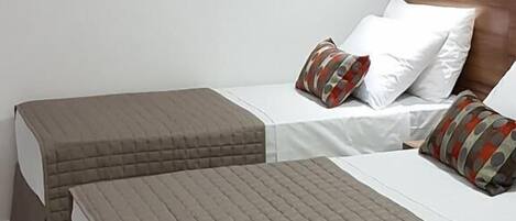 A hotel room with two beds, each with a quilted headboard and pillows.