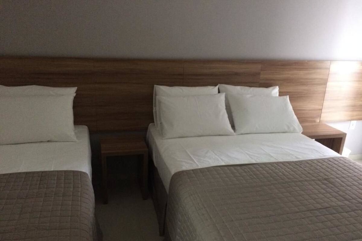 Habitación de hotel con dos camas, un cabecero de madera y una mesita de noche con una lámpara.
