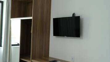 A room with a wooden desk, a white chair, a television mounted on the wall, and a small refrigerator.