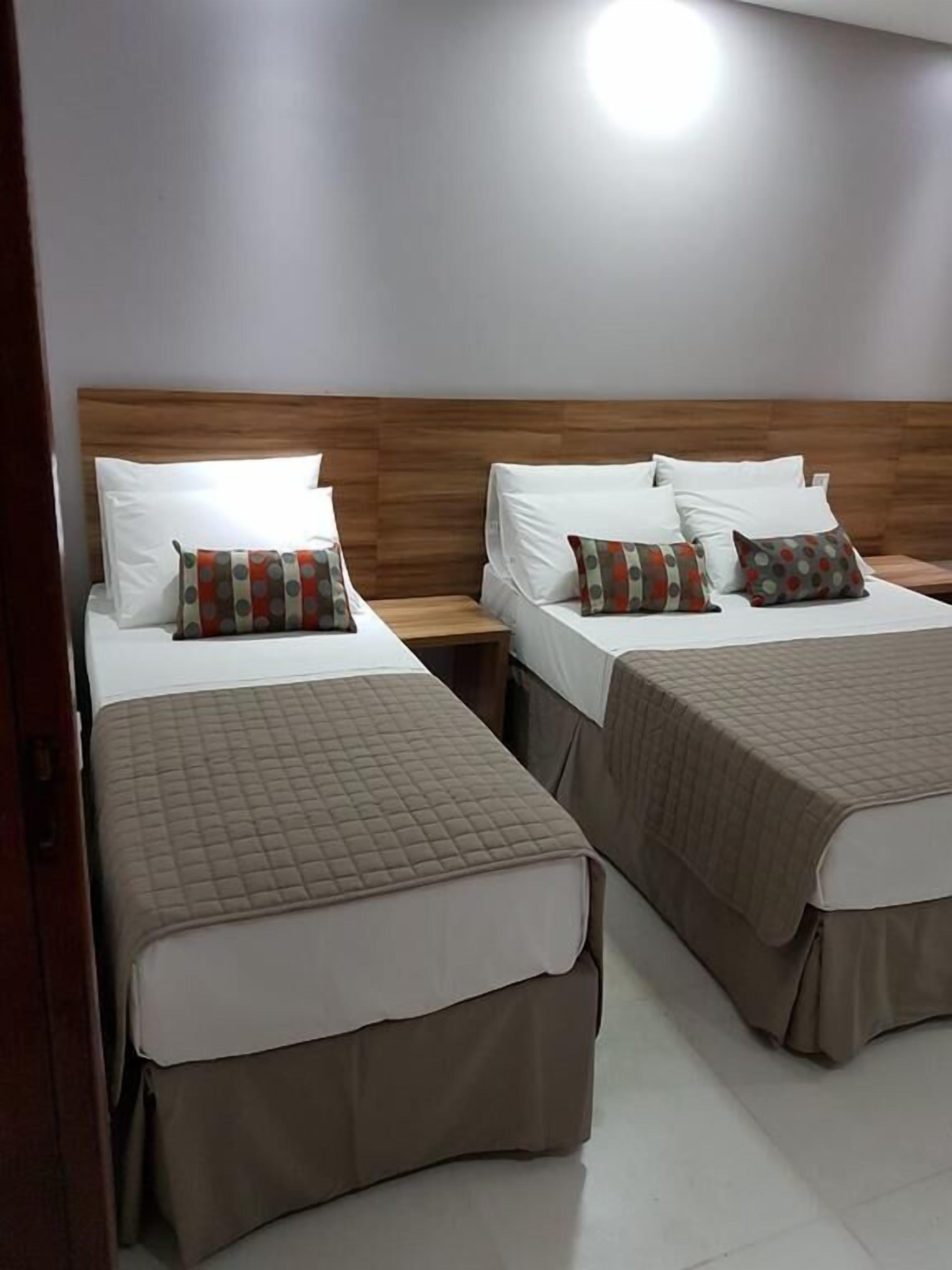 A hotel room with two beds, each with a wooden headboard and white bedding.