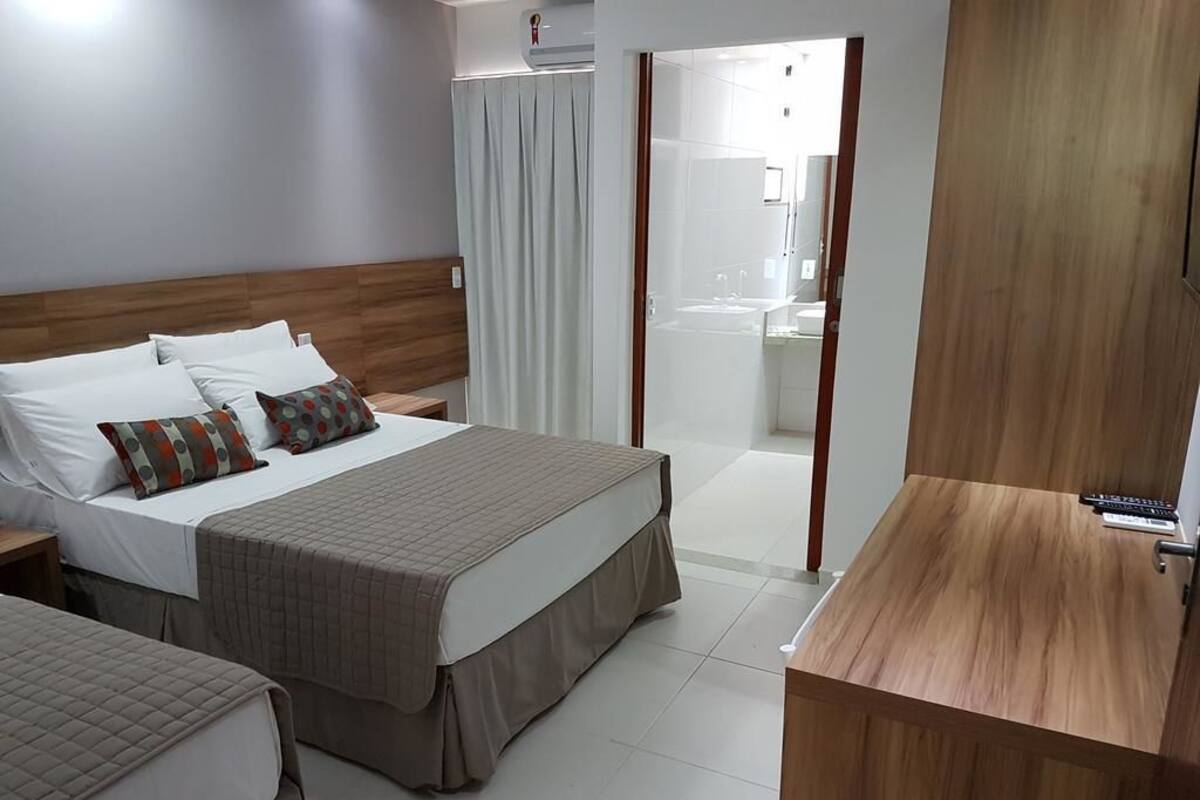 Habitación de hotel con dos camas, cabecero de madera, un escritorio pequeño y baño visible a través de una puerta de vidrio.
