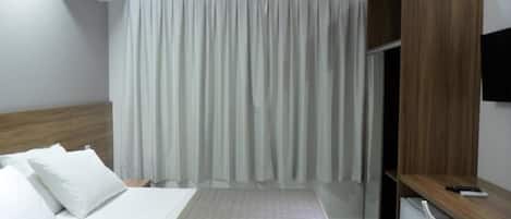 Una habitación de hotel con cama, escritorio, silla, armario y equipo de aire acondicionado.